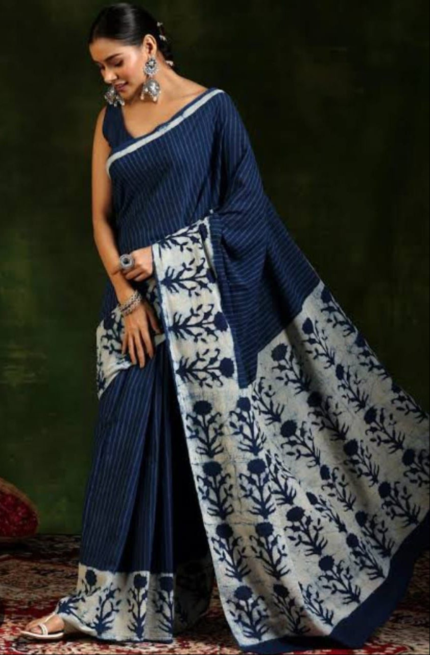 Woman wearing a blue and white saree with a floral pattern against a dark background